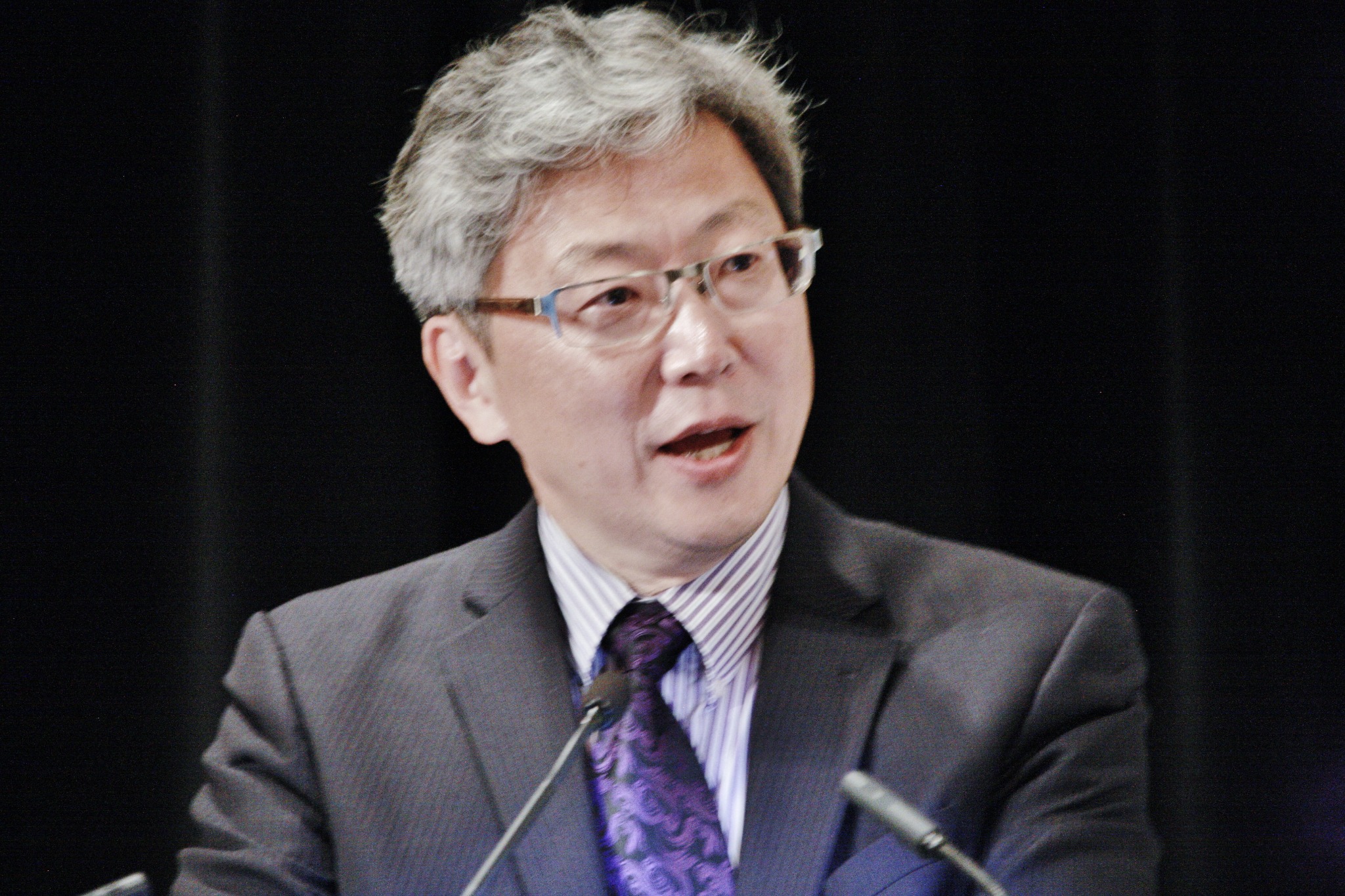 Close view of Michael Hwang speaking in front of two microphones